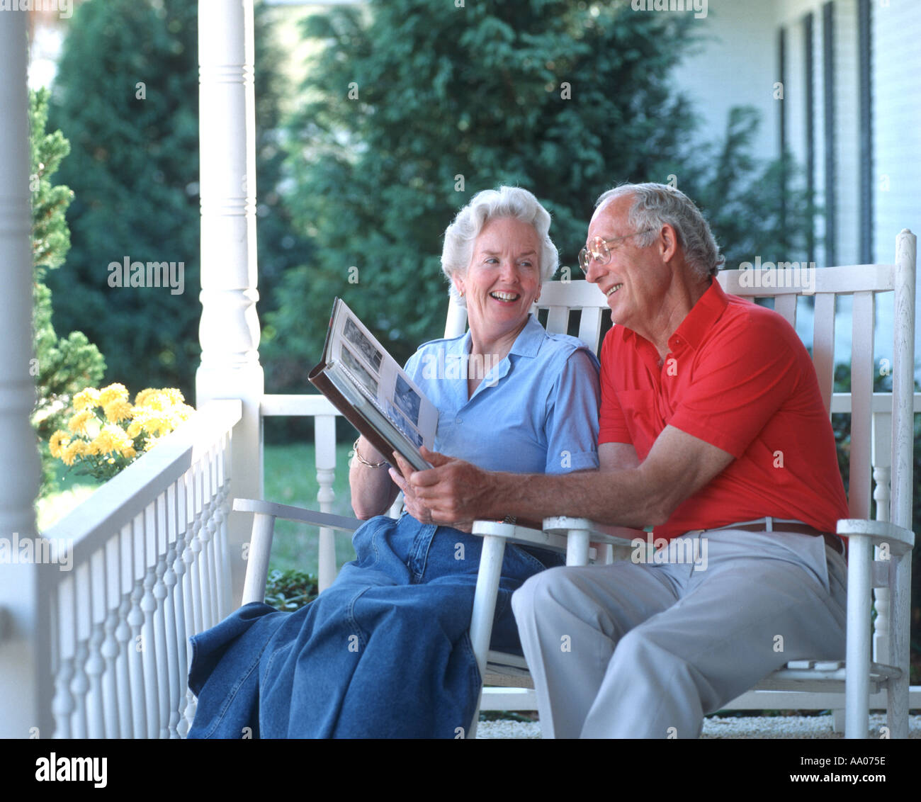 mature couple sitting in rocking chairs on porch looking at photo album Stock Photo