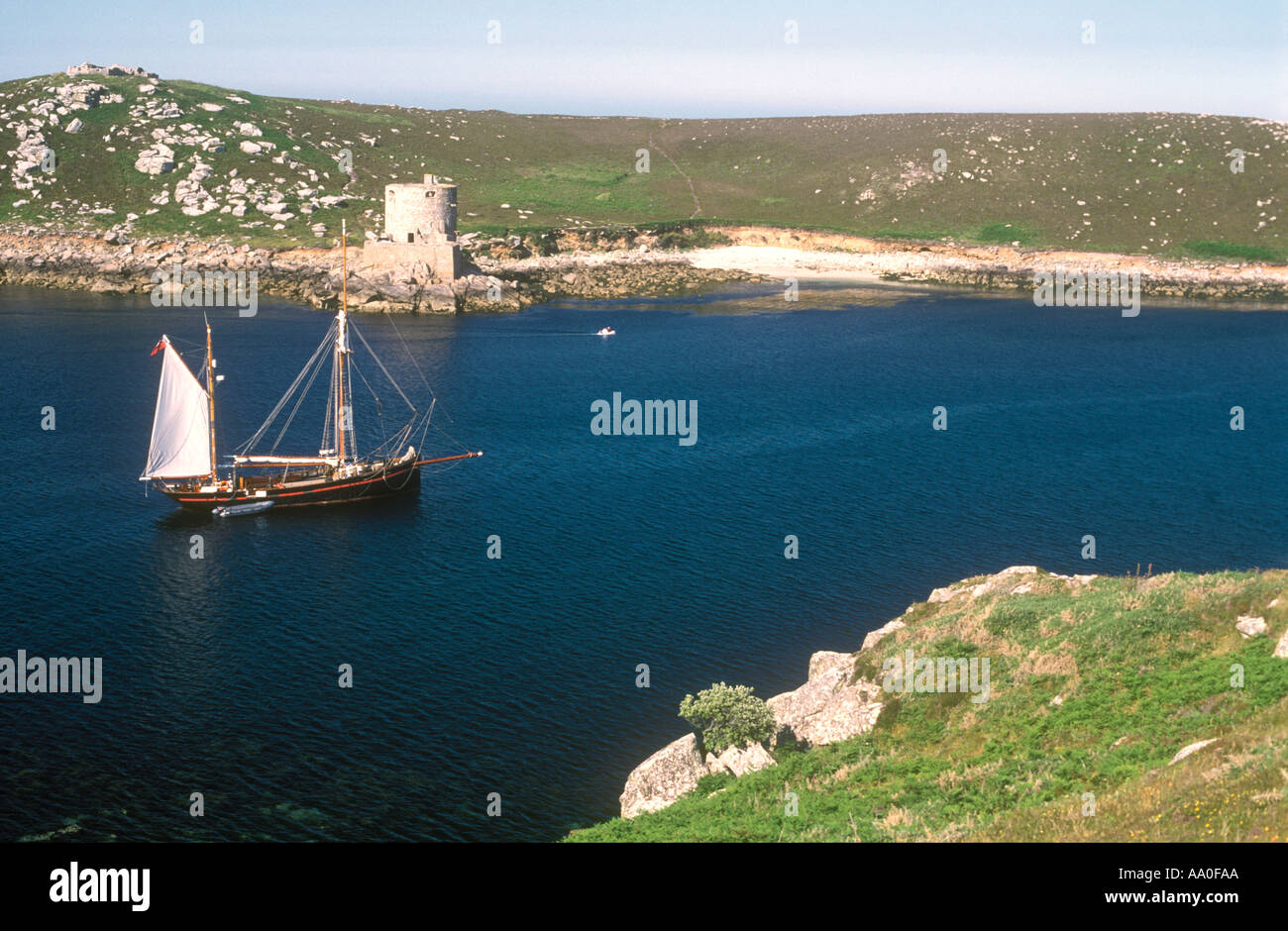 View from Bryher of schooner in Tresco Channel,  looking to Tresco Island  & Cromwell's Castle, Isles of Scilly, Cornwall, UK Stock Photo