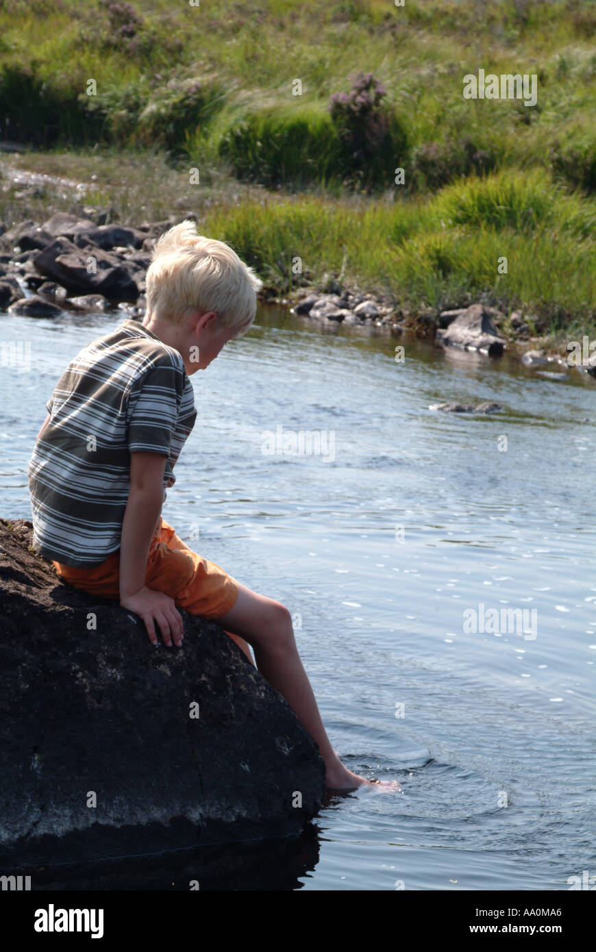 Little boy sitting on a rock with feet immersed in a river Stock Photo ...