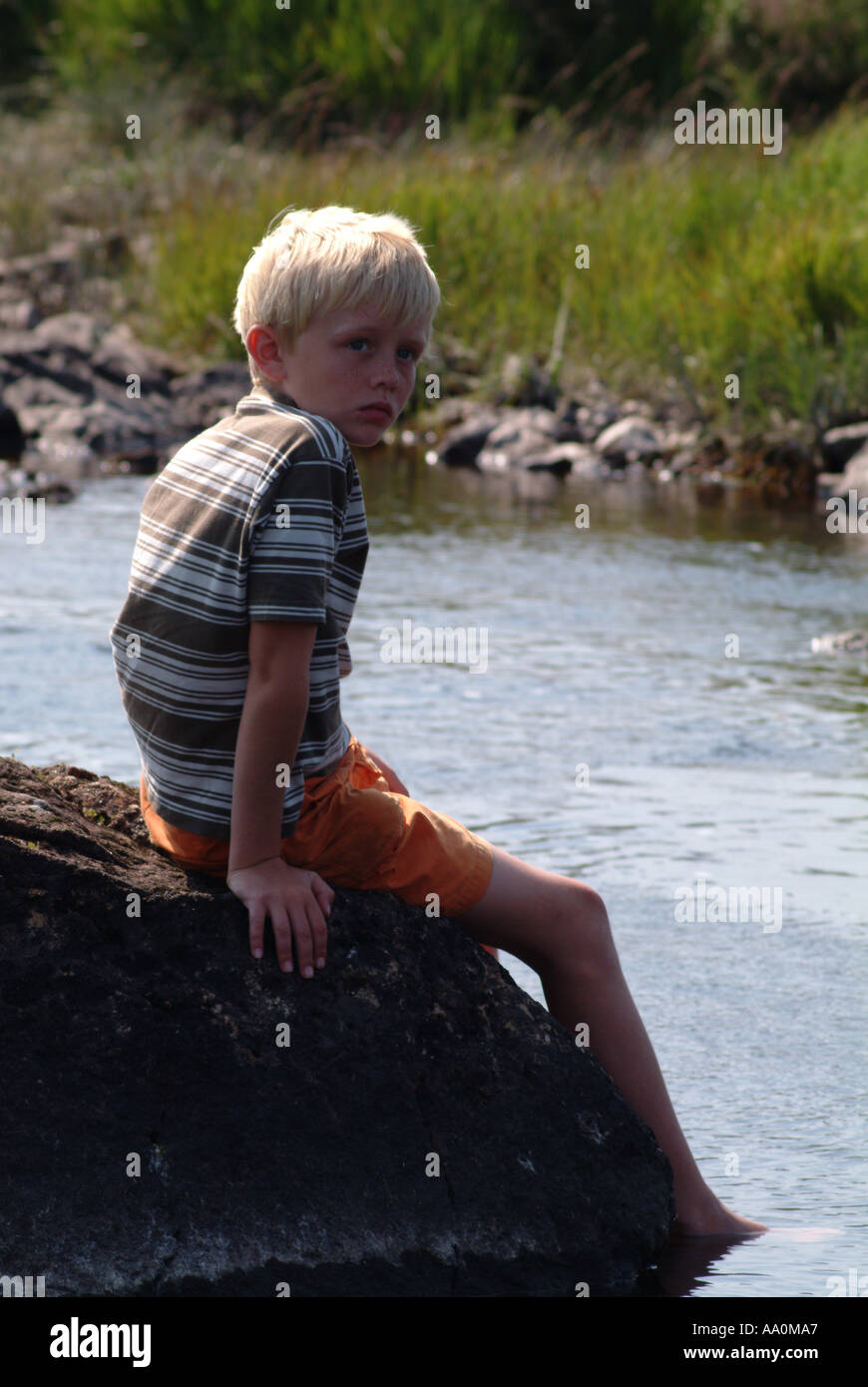 Little boy sitting on a rock with feet immersed in a river Stock Photo ...