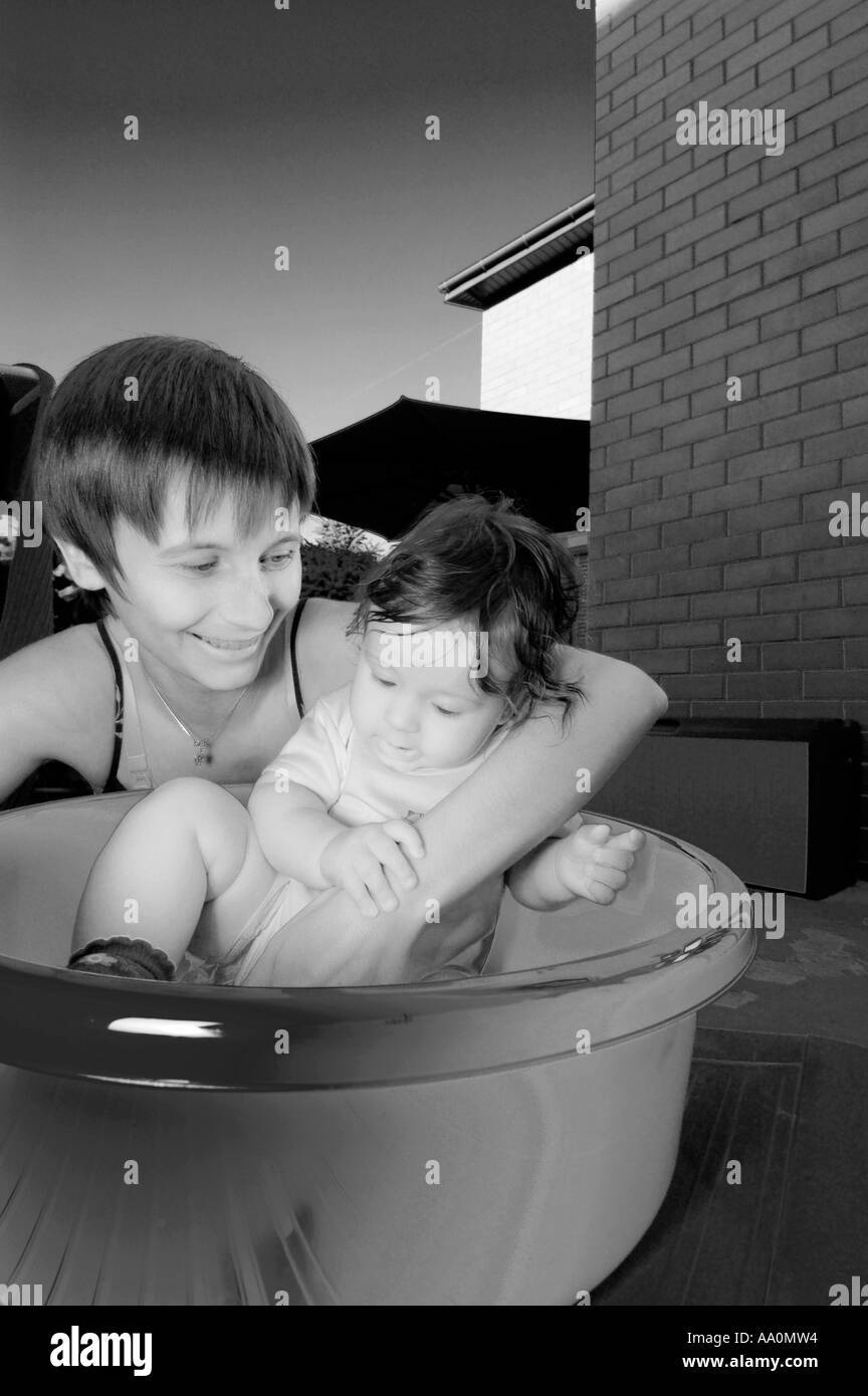 Poland, mother assisting baby girl (6-9 months) sitting in washing tub (B&W) Stock Photo