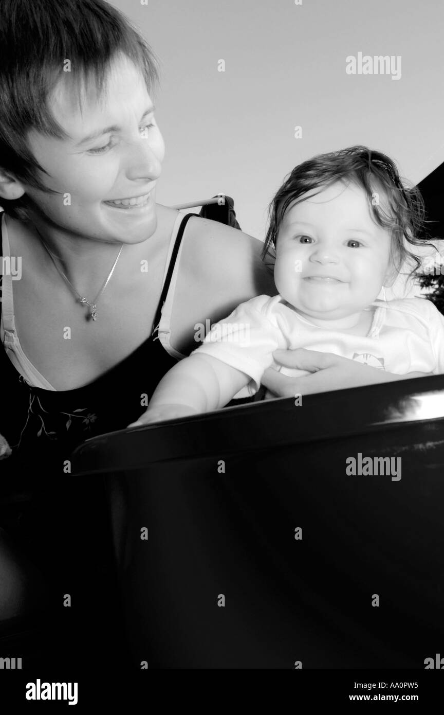 Poland, mother assisting baby girl (6-9 months) sitting in washing tub, portrait (B&W) Stock Photo
