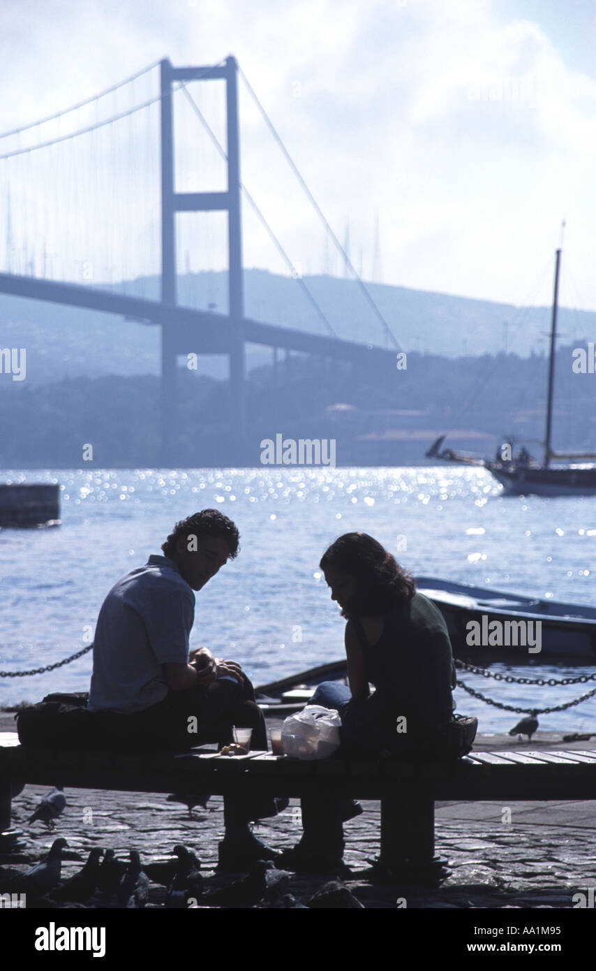 ISTANBUL. A young couple eating a picnic lunch by the Bosphorous at Ortakoy, with the first Bosphorus Bridge behind. 2006. Stock Photo