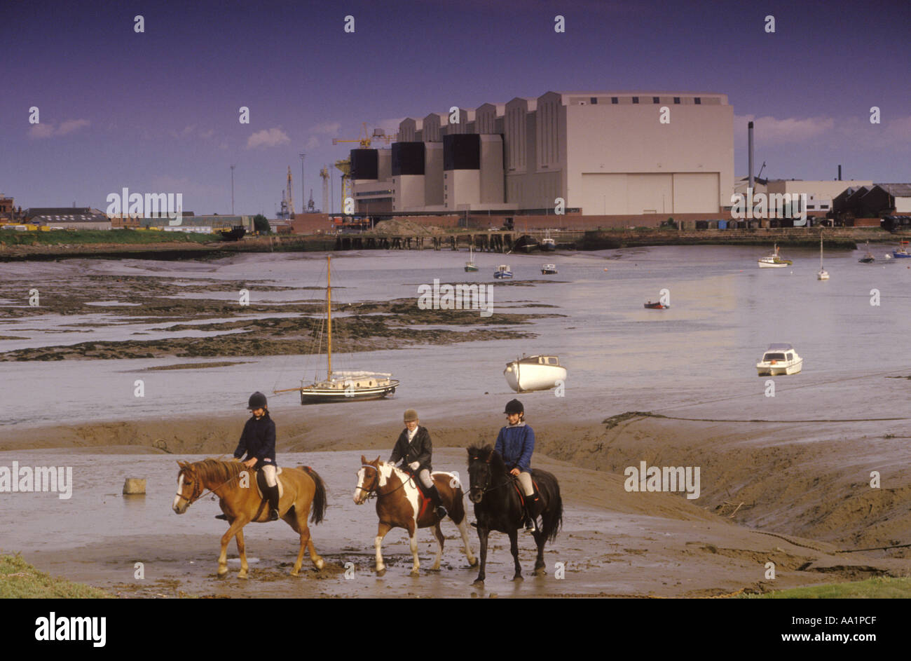 Children on ponies horses with shipyard in the distance Barrow in Furness Cumbria. Taken from Walney Island, across Walney Channel UK 1980s 80s HOMER Stock Photo