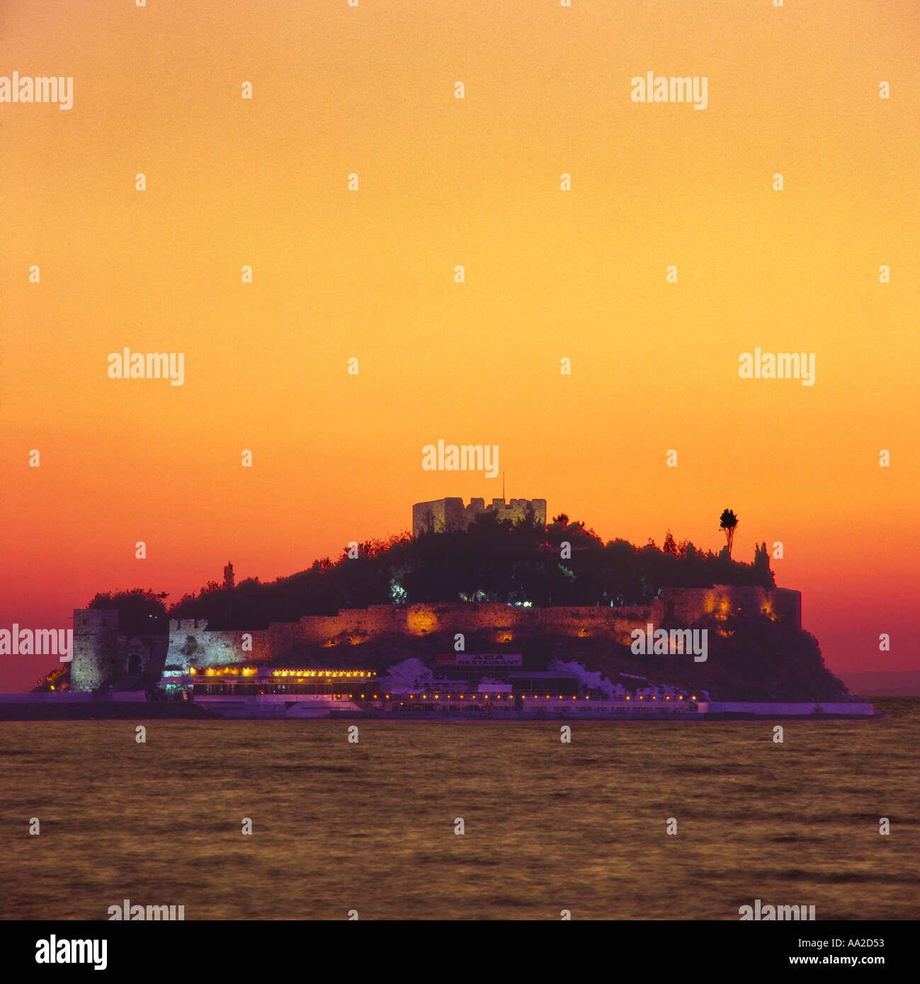 The illuminated castle fortress atop island promontory of Guvercin Adasi or Pigeon Island silhouetted at sunset Kusadasi Turkey Stock Photo