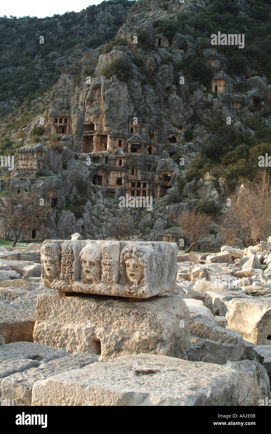 Frieze of stone masks from ancient theatre with rock-cut tombs in  background, Myra Stock Photo