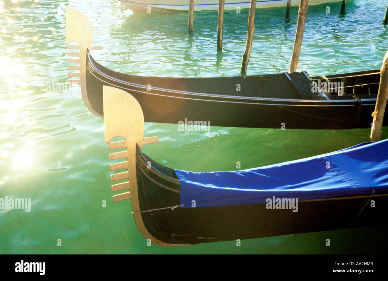 Italy, Venice, gondolas in sun on water surface Canale Grande Grand Canal, carved prows of gondolas moored by canal Stock Photo
