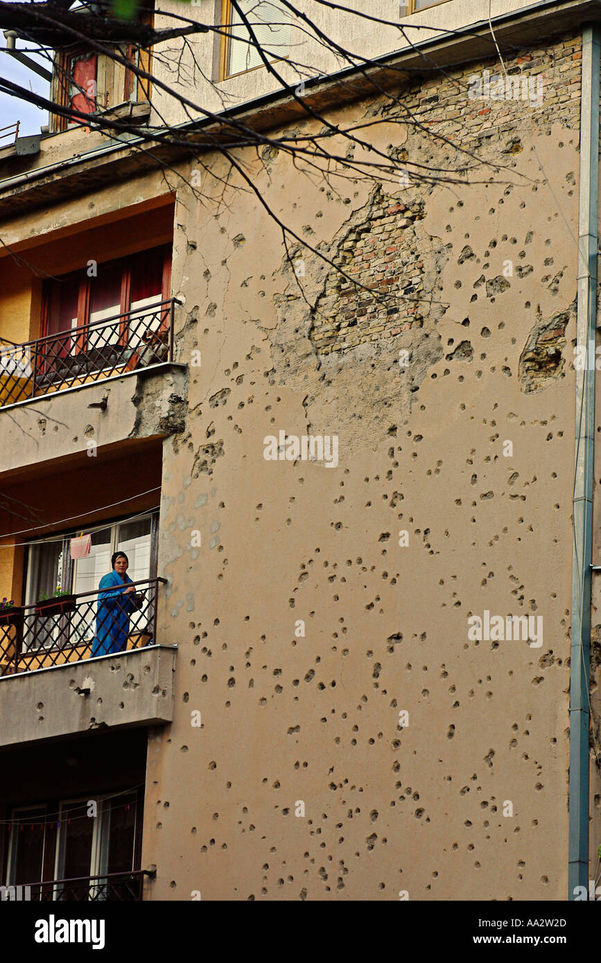 a woman looking off her balcony an apartment building scarred during the war in Sarajevo Stock Photo