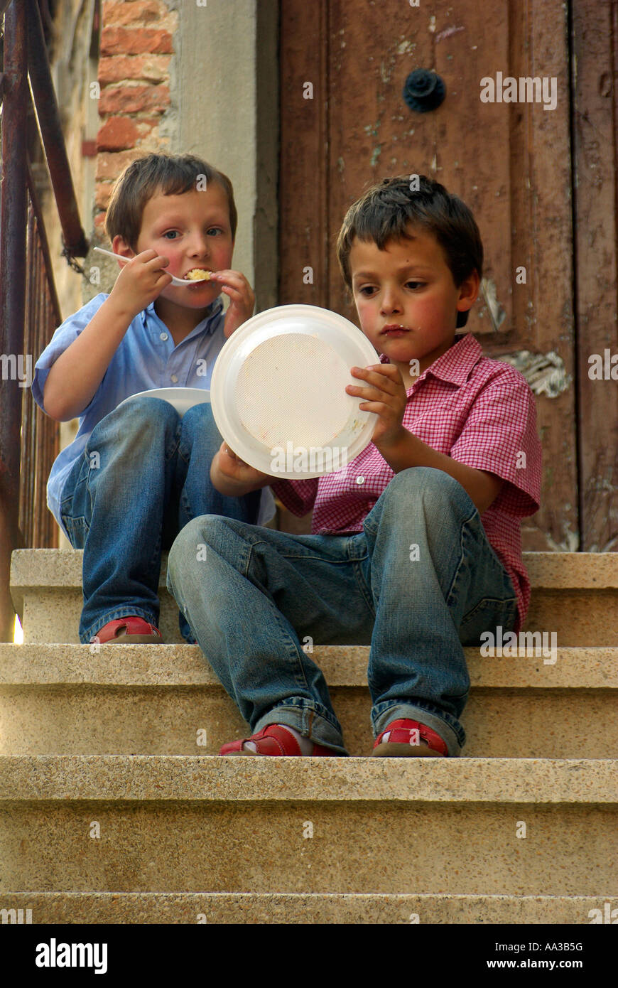 Two boys eat cake from plastic plates on steps in rural Italy Stock Photo