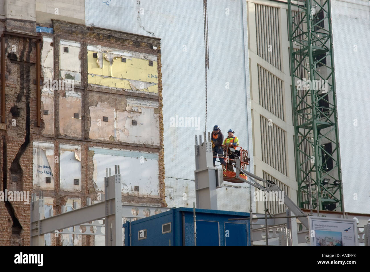 Two construction workers wearing protective helmets being raised in moving cage on building site, London, UK, 2006 Stock Photo