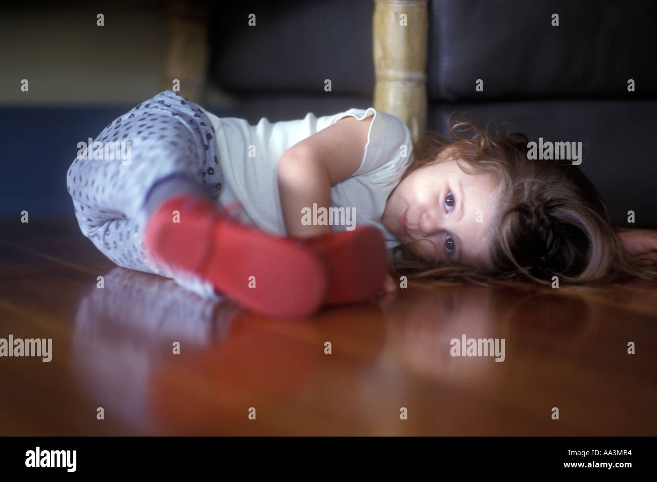1 2 0ne to two years old kid laying on hard wood floor under furniture at home Stock Photo
