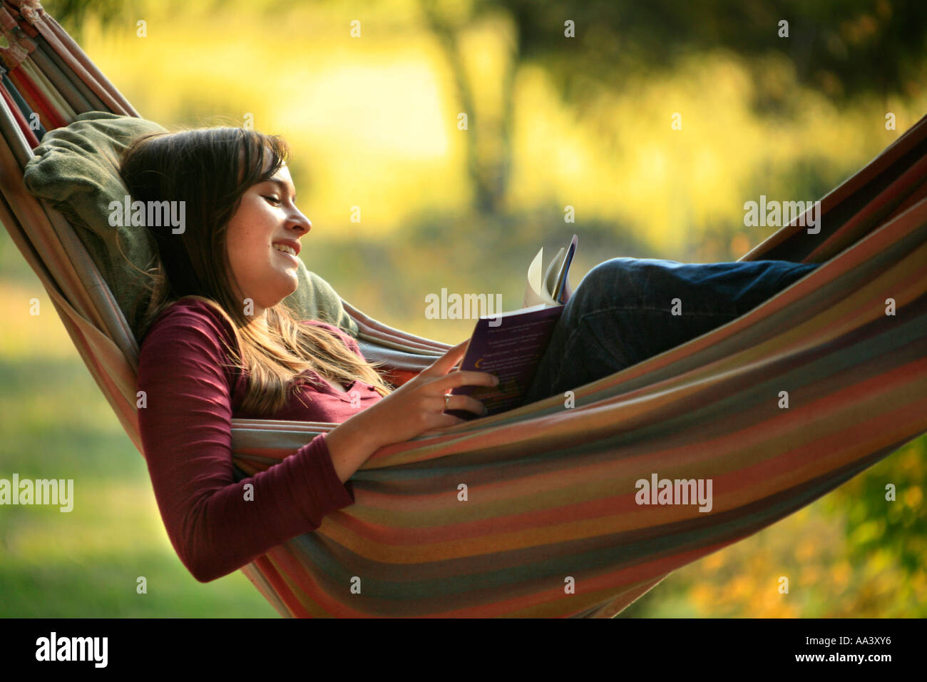 A young teen-aged girl reads a book in a hammock at sunset. Stock Photo