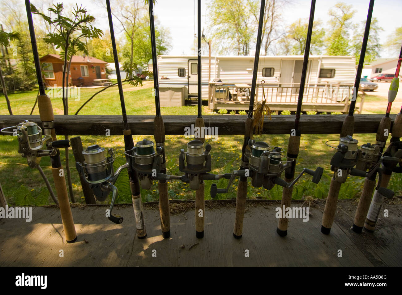 ABU GARCIA FISHING POLES AND SPINNING REELS STAND IN A ROW ON A DECK WITH A CAMPER TRAILER IN THE BACKGROUND AT A LAKE RESORT Stock Photo