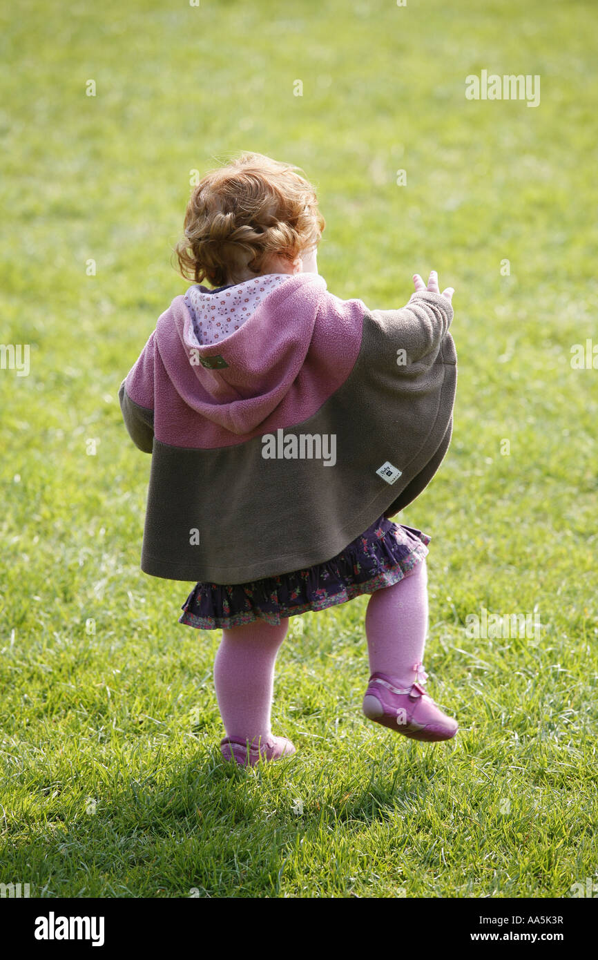 Rear of a one year old baby toddler learning how to walk in a park