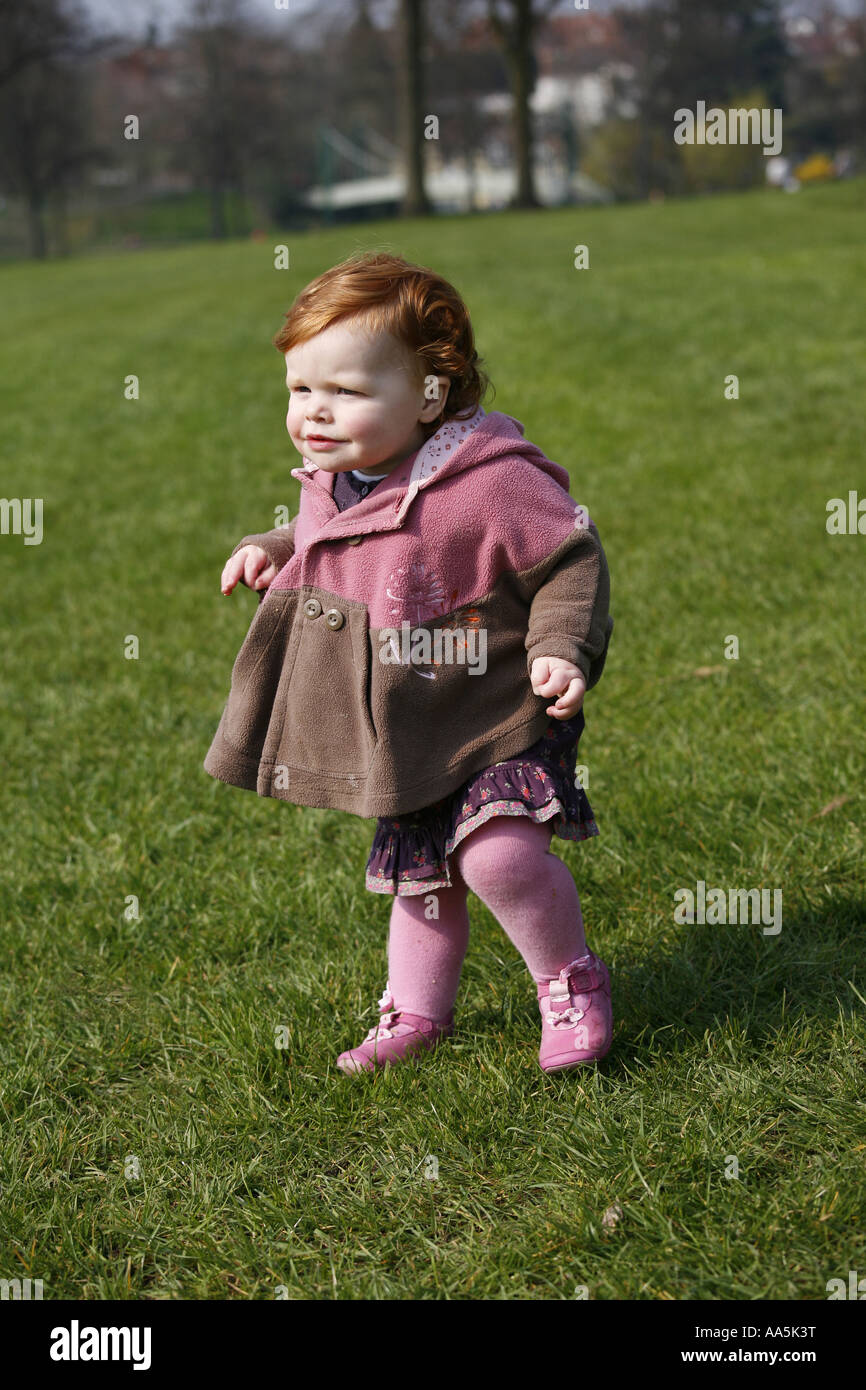 A one year old baby toddler learning how to walk in a park Stock Photo