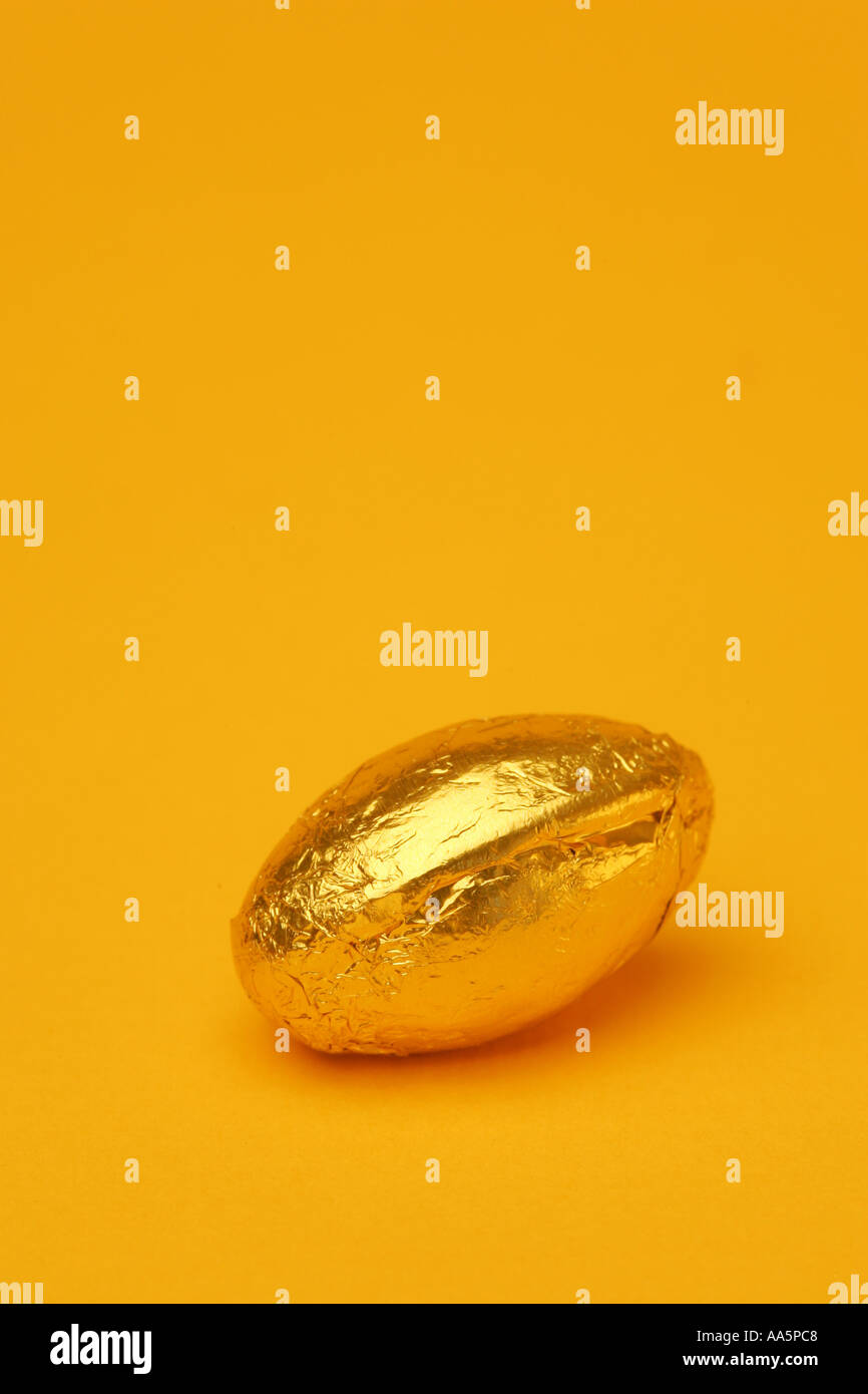 One 1 single bright coloured golden Easter egg in foil wrapper chocolate confectionary with a seasonal Spring yellow background Stock Photo