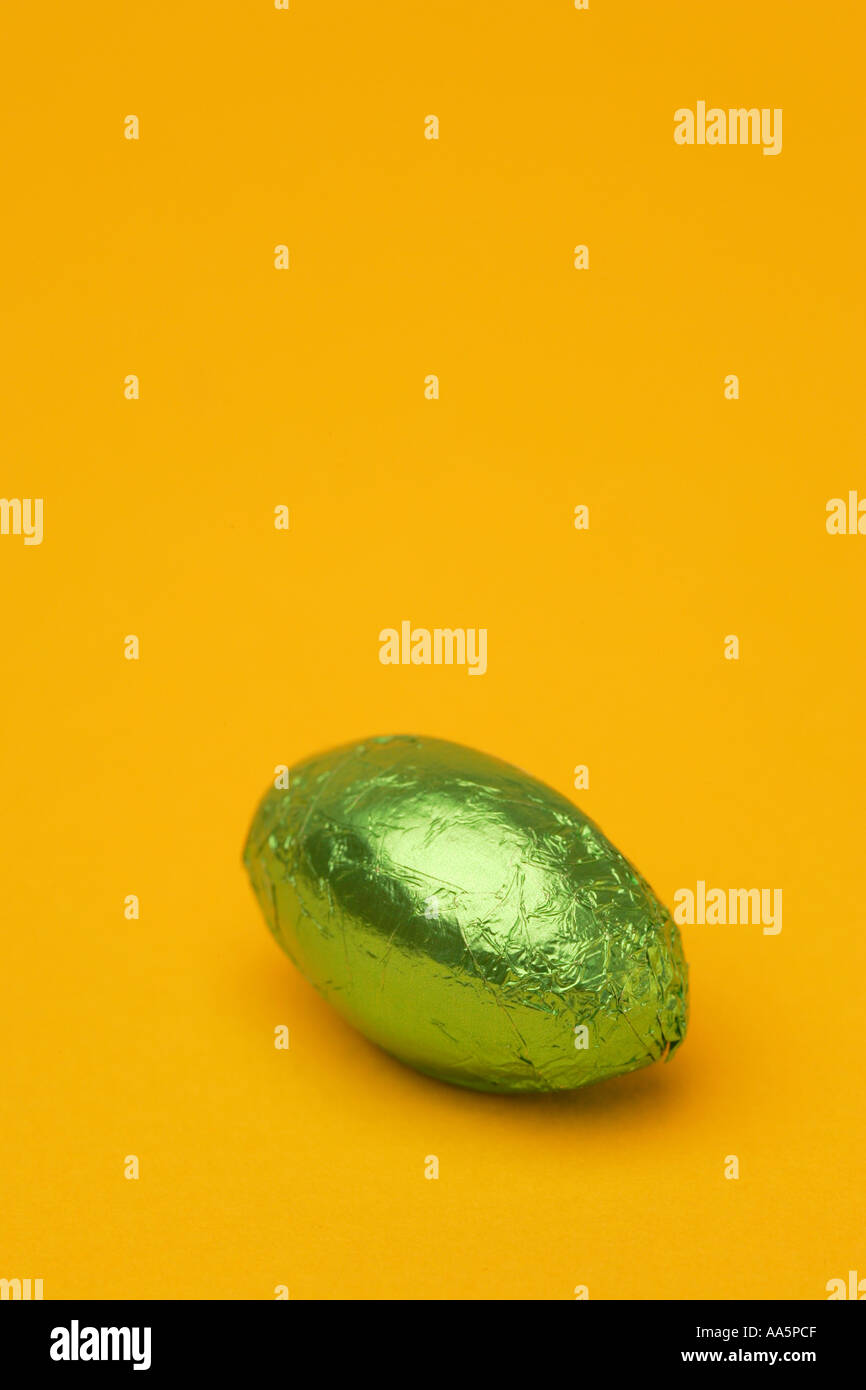 One 1 single bright coloured green Easter egg in foil wrapper chocolate confectionary with a seasonal Spring yellow background Stock Photo
