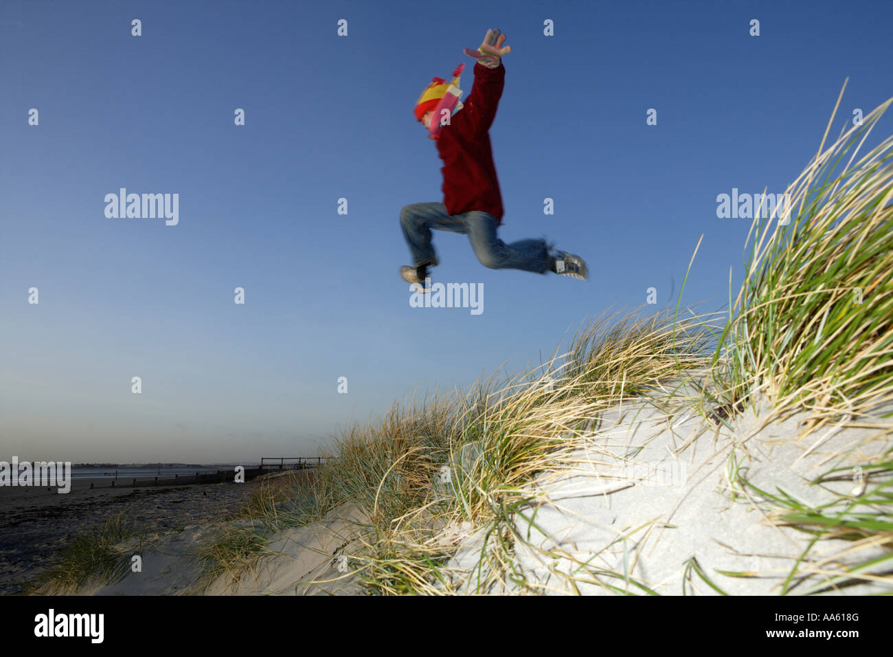 Child jumping off sand dunes in Winter West Wittering beach West Sussex