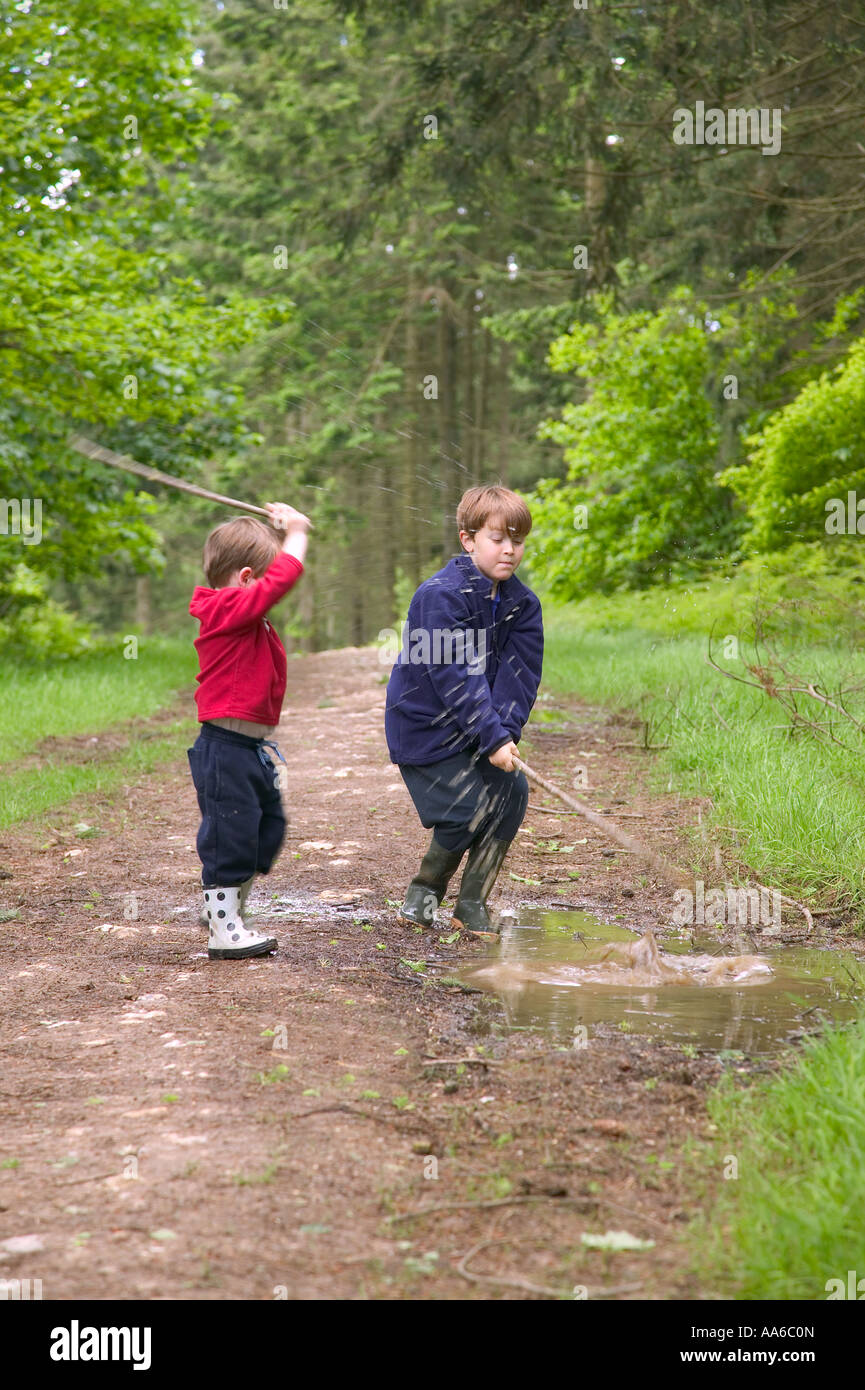 Two young brothers having fun splashing in a muddy puddle Stock Photo