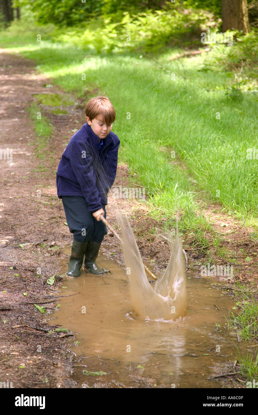 Young boy having fun splashing in a muddy puddle in the woods Stock Photo