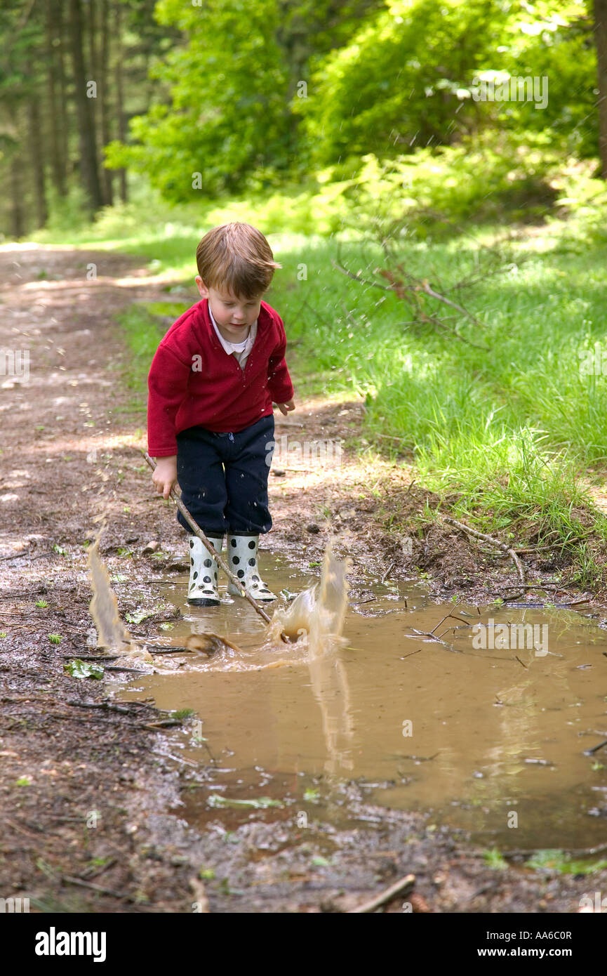 Toddler splashing in a muddy puddle with his stick Stock Photo