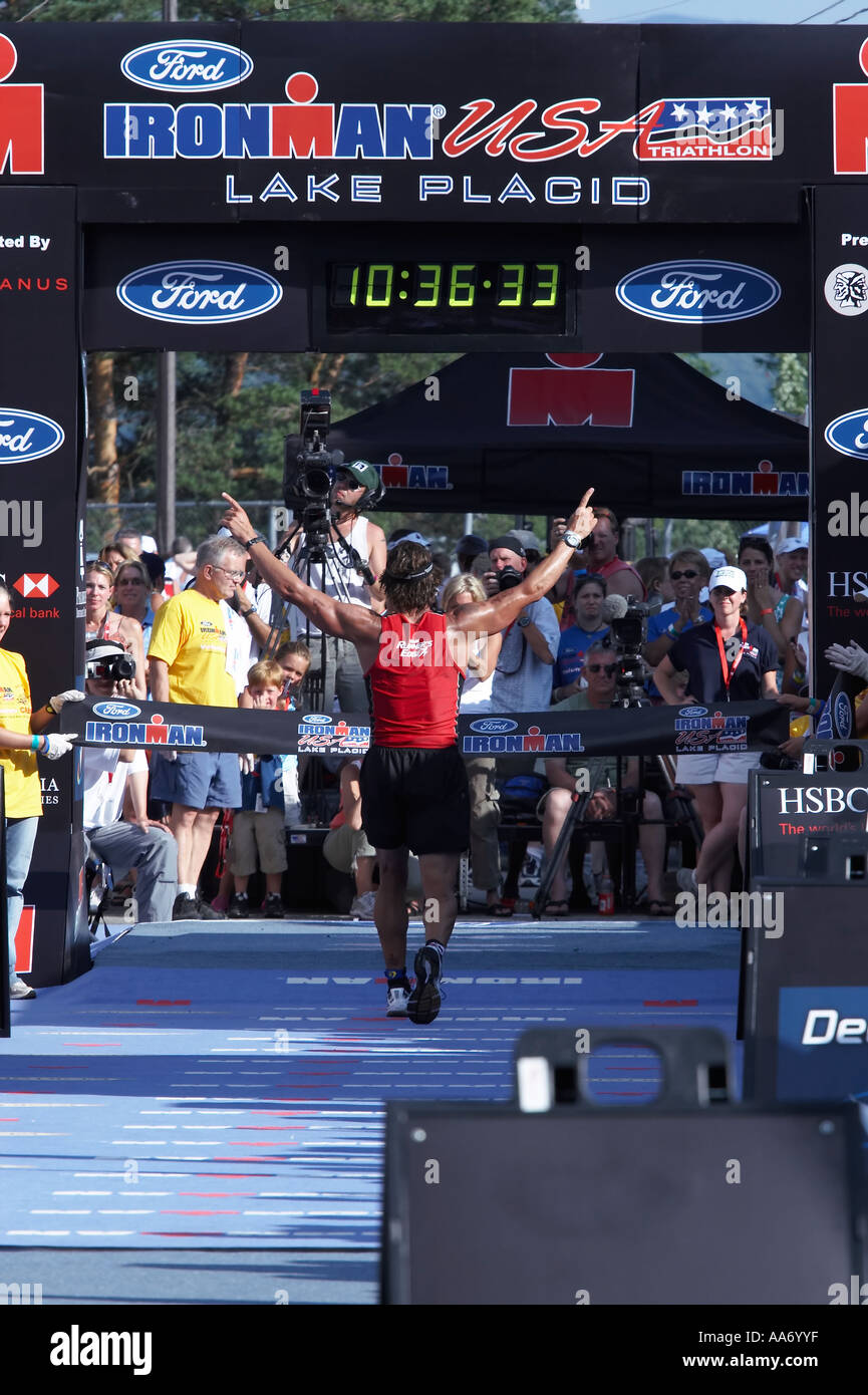 A competitor of Ironman Lake Placid raising his arms as he crosses the finish line Stock Photo