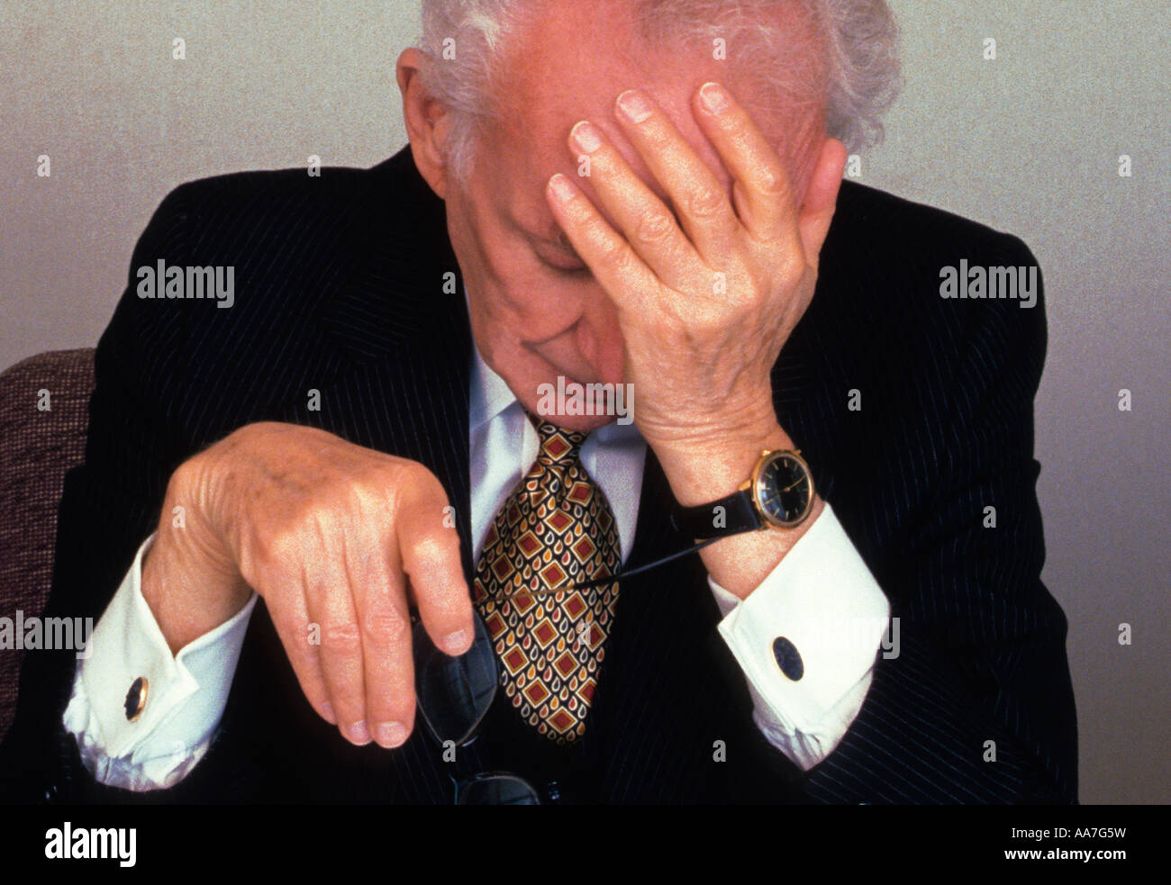 elderly tired discouraged formally well dressed businessman alone in office with his hand to his head Stock Photo