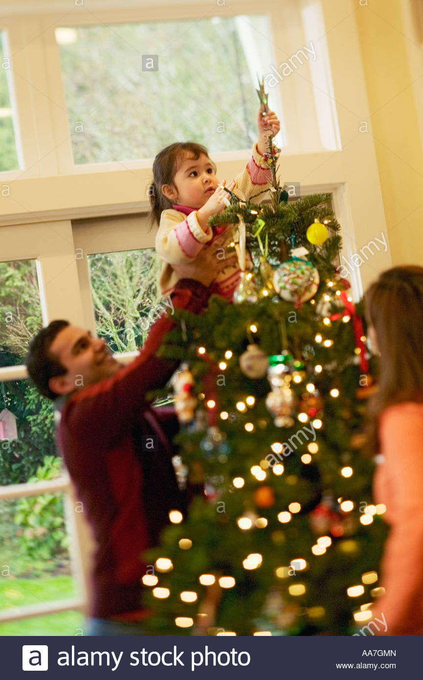Father helping toddler girl putting star on Christmas tree Stock Photo
