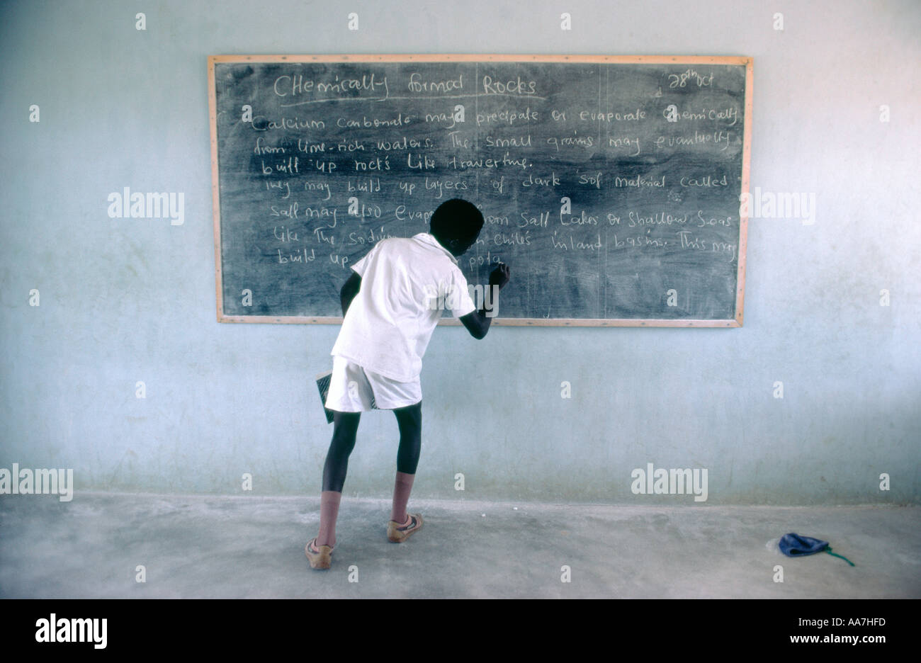 Nigerian schoolboy writing on chalk blackboard in classroom during geology lesson. Nigeria Stock Photo