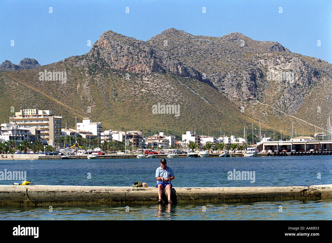 A tourist fishes on a walkway off the beach at Puerto Pollensa in Majorca Stock Photo