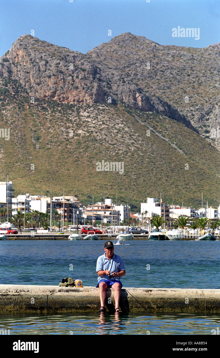 A tourist fishes on a walkway off the beach at Puerto Pollensa in Majorca Stock Photo