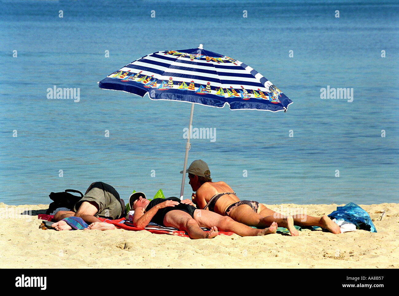 Tourists sunbathe by a beach umbrella at Puerto Pollensa in Majorca Stock Photo
