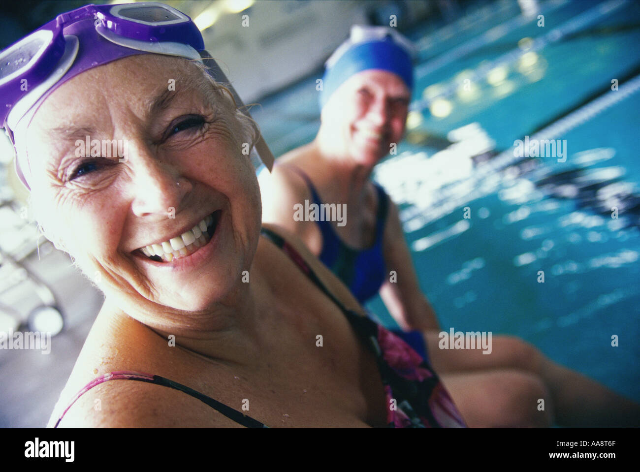Portrait of two senior women sitting at the edge of a swimming pool ...