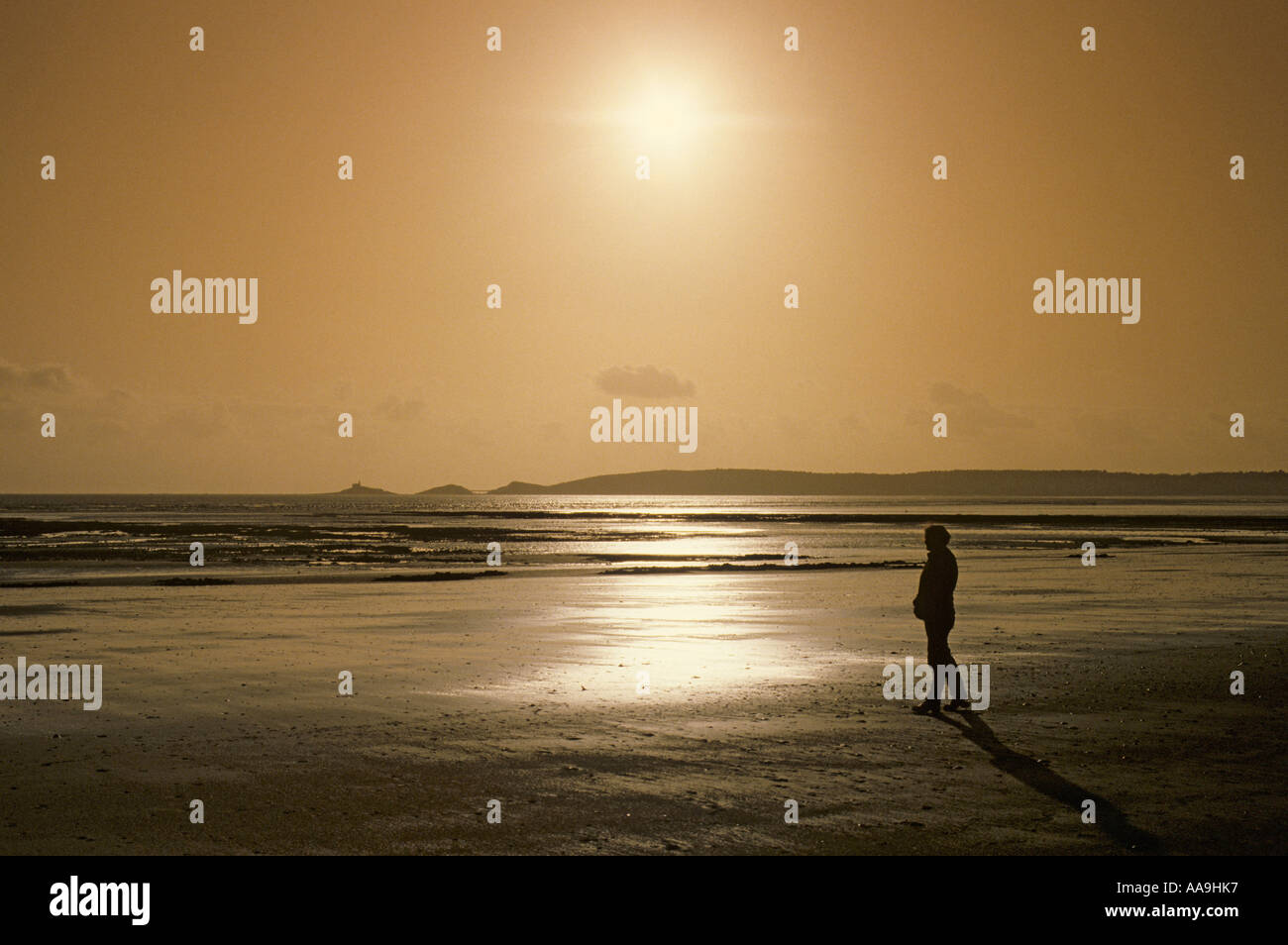Woman walking alone on Swansea beach with the Mumbles in the distance Wales UK Stock Photo
