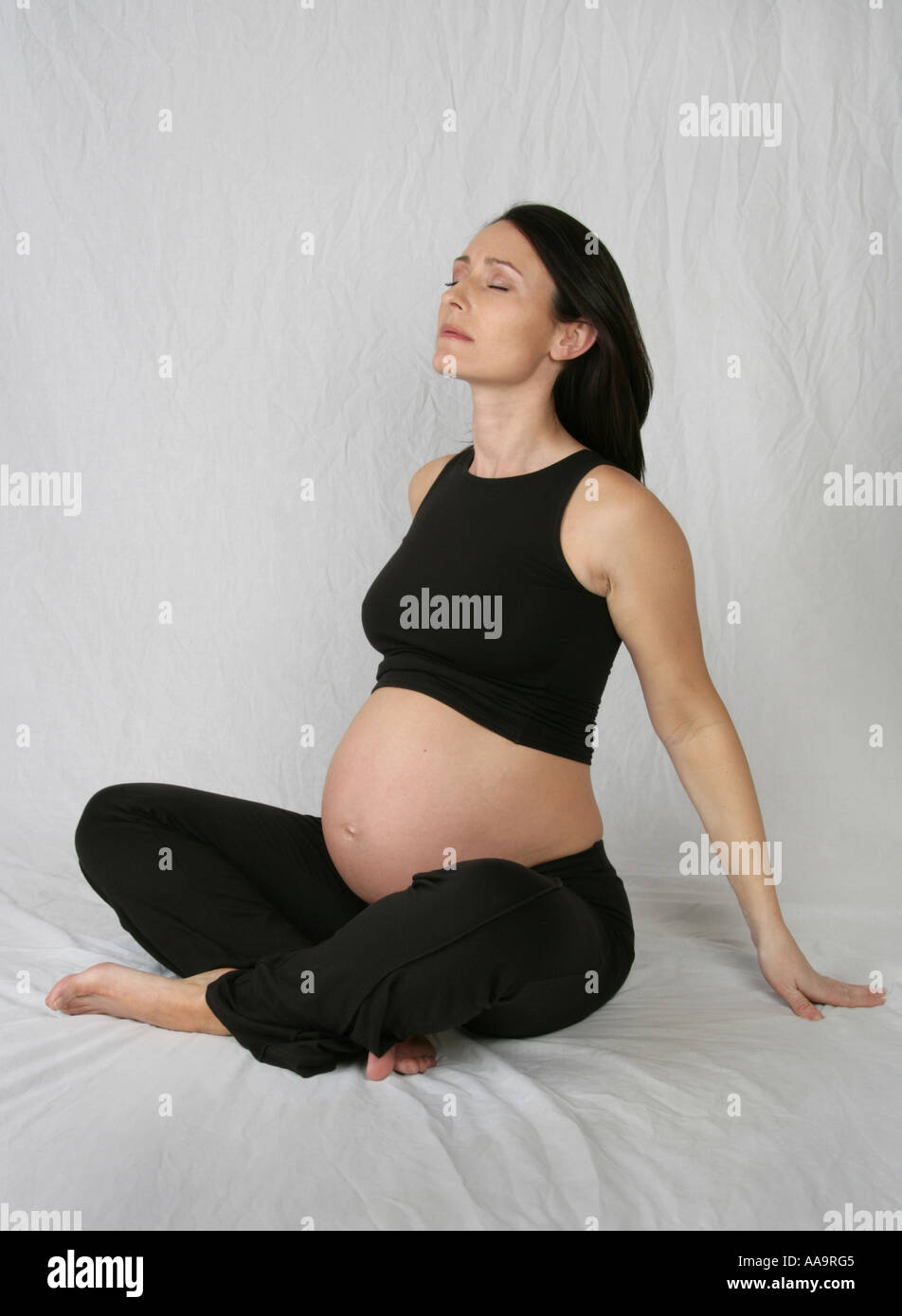 Pregnant Woman Sitting Crossed Legged Wearing a Black Vest and Trousers Stock Photo