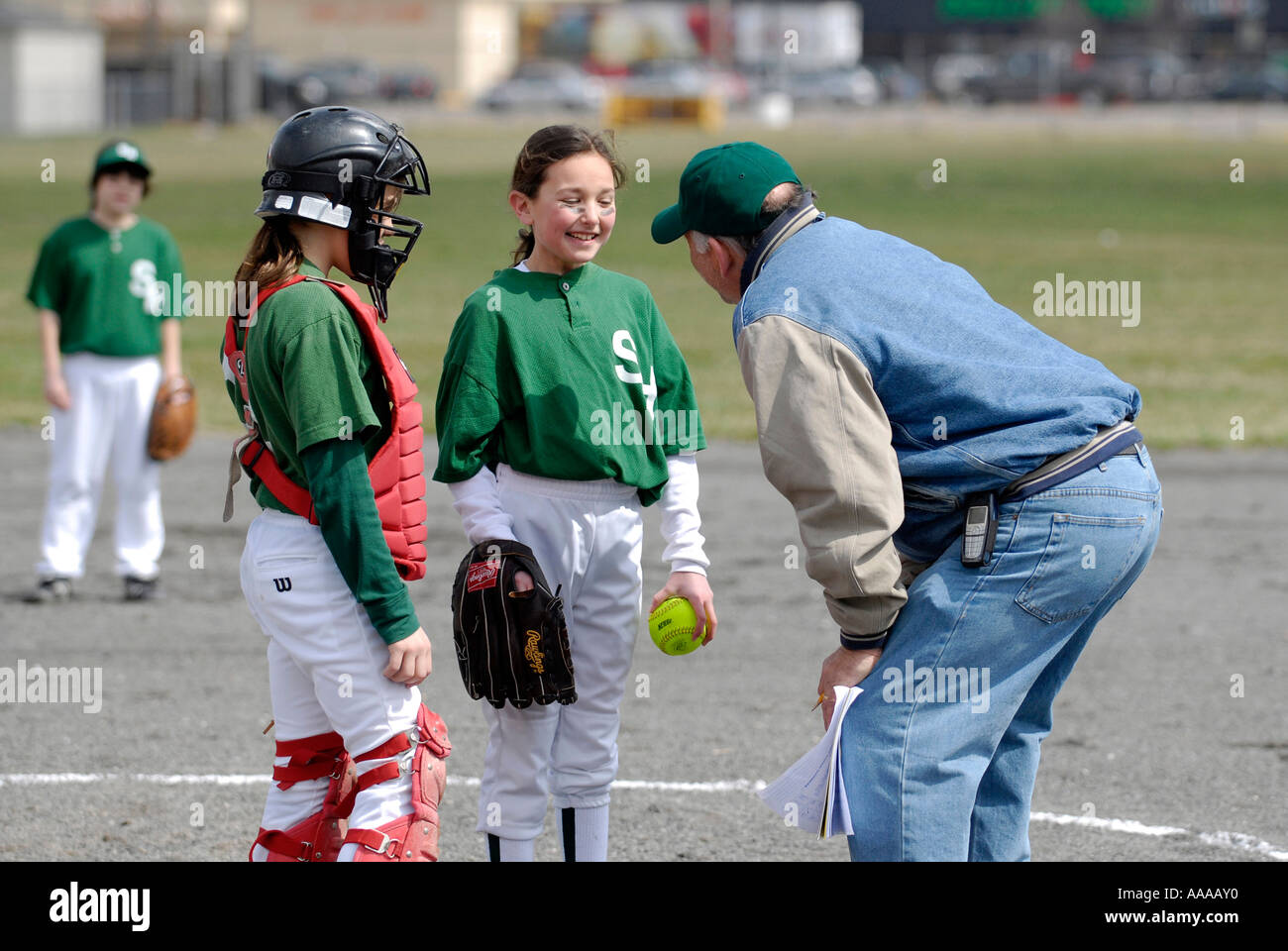 Young girls play softball with coach talking with the pitcher Stock Photo