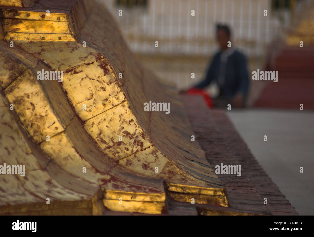 Myanmar Burma Yangon Shwedagon Paya close up of golden basis of a stupa with man praying in bkgd Stock Photo