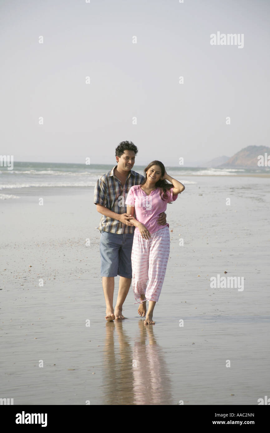 South Asian Indian young man and woman holding hands walking together on seashore; Shiroda; Dist. Sindhudurga; Maharashtra; Indi Stock Photo