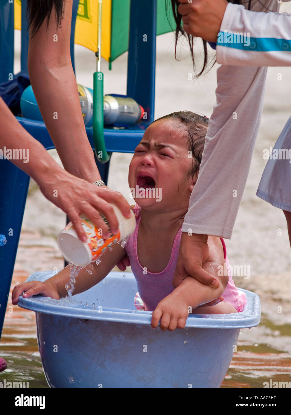 baby cries while getting a curbside bath during the Lao Songkran New