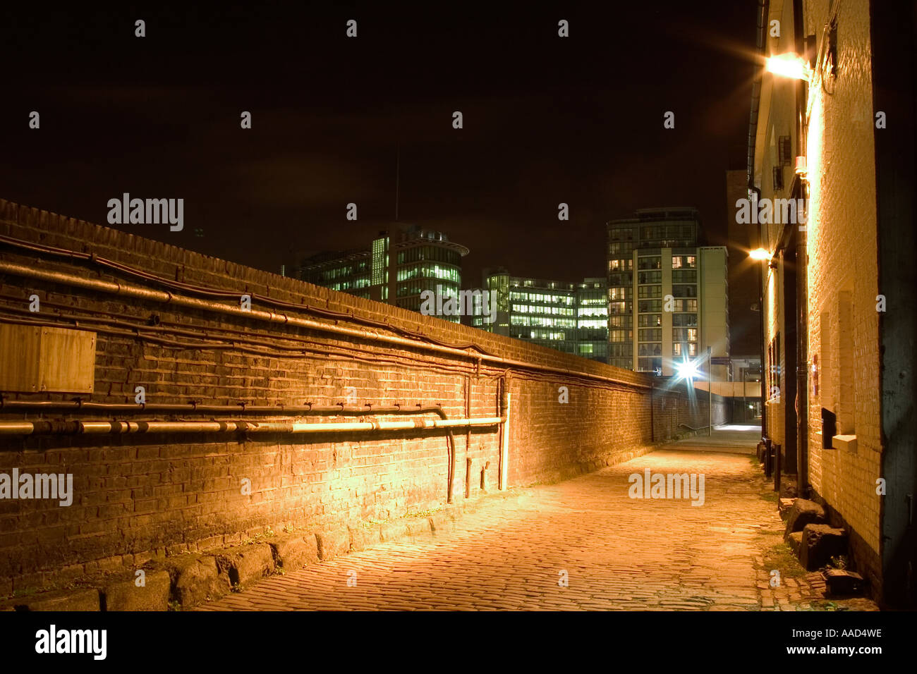 Cobbled alley at night behind St Mary's Hospital with Paddington Basin Offices in background. London, England Stock Photo