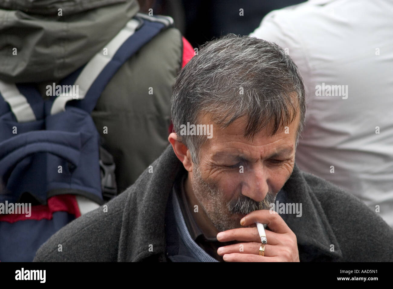 Unshaven man smoking cigarette in crowd. Trafalgar Square, London England Stock Photo