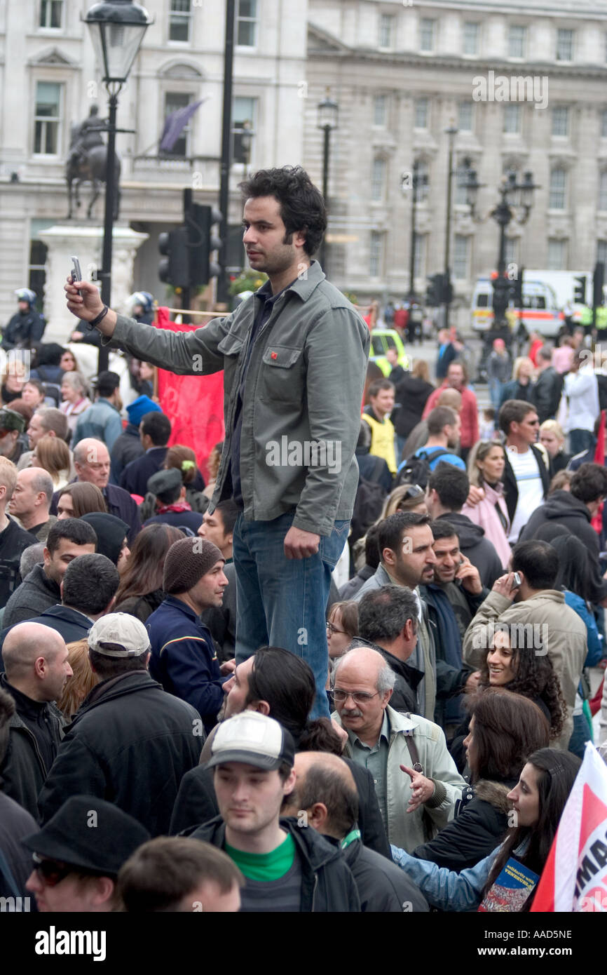 Man standing above crowd taking photograph on mobile phone during Mayday demonstration. Trafalgar Square, London, England Stock Photo
