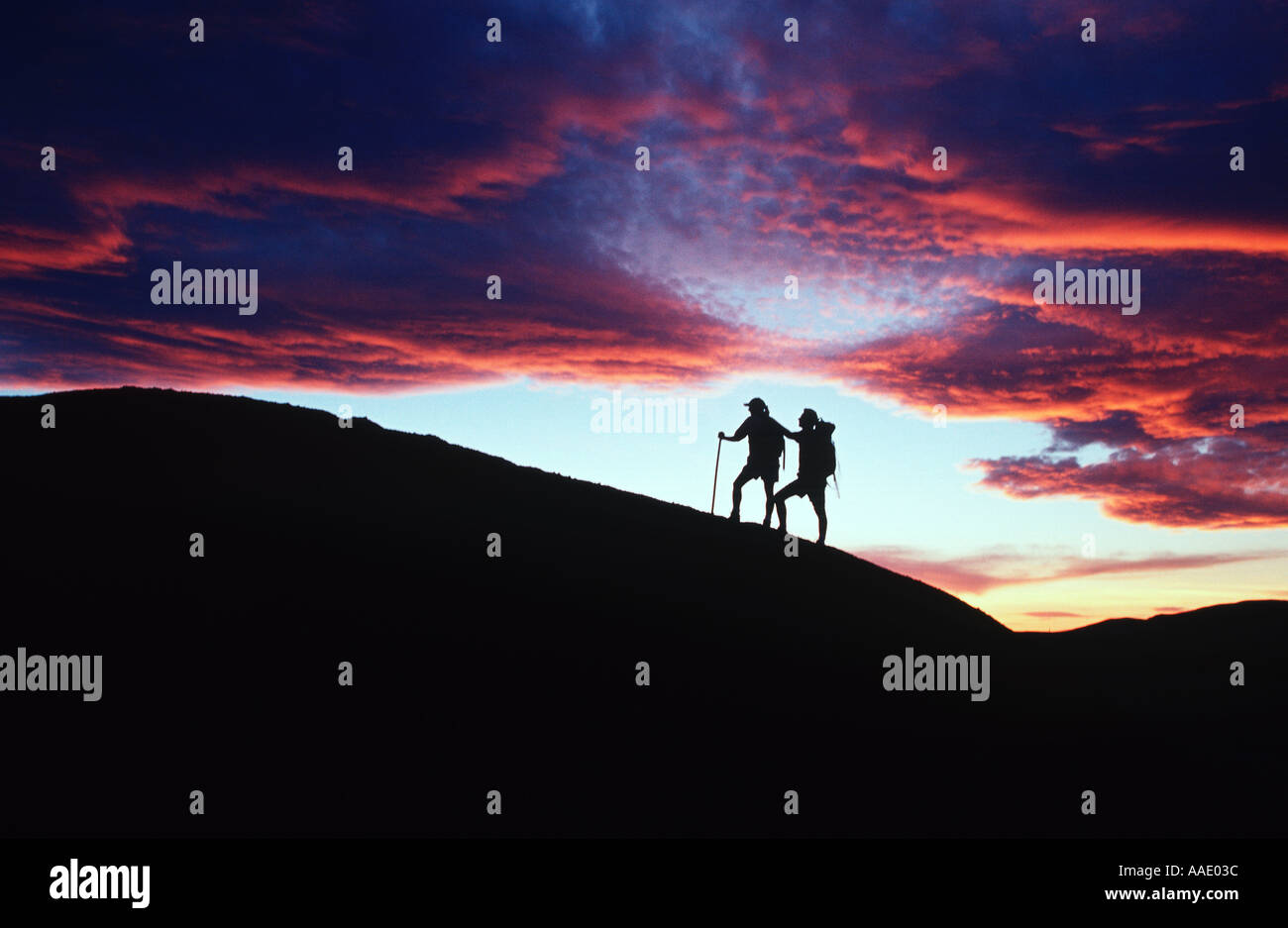 Hikers continue their journey silhouetted against a colorful evening sky Stock Photo