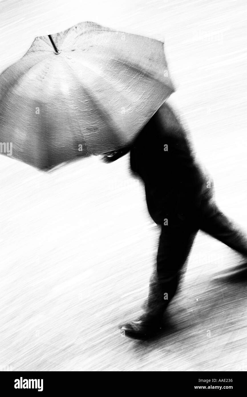A business man in suit walking at speed under an umbrella in the rain ...