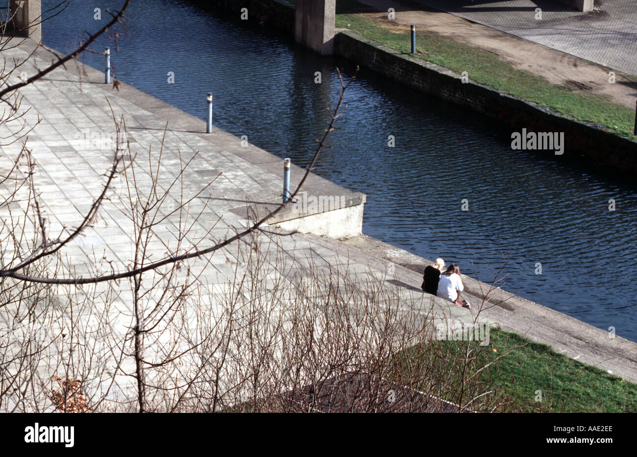 Two people stting by a canal in a northern town in England in winter sunlight Stock Photo