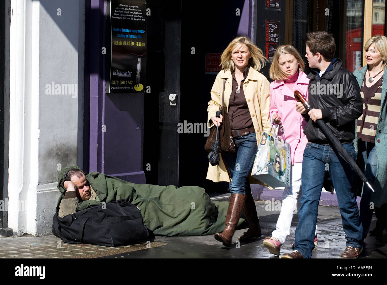 Young affluent family walk past homeless man London Stock Photo