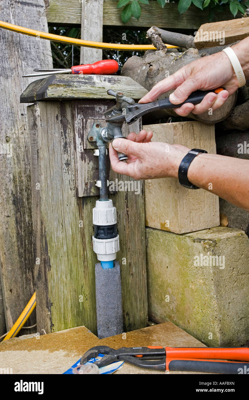 Hands with spanner repairing leaking outside garden tap UK Stock Photo