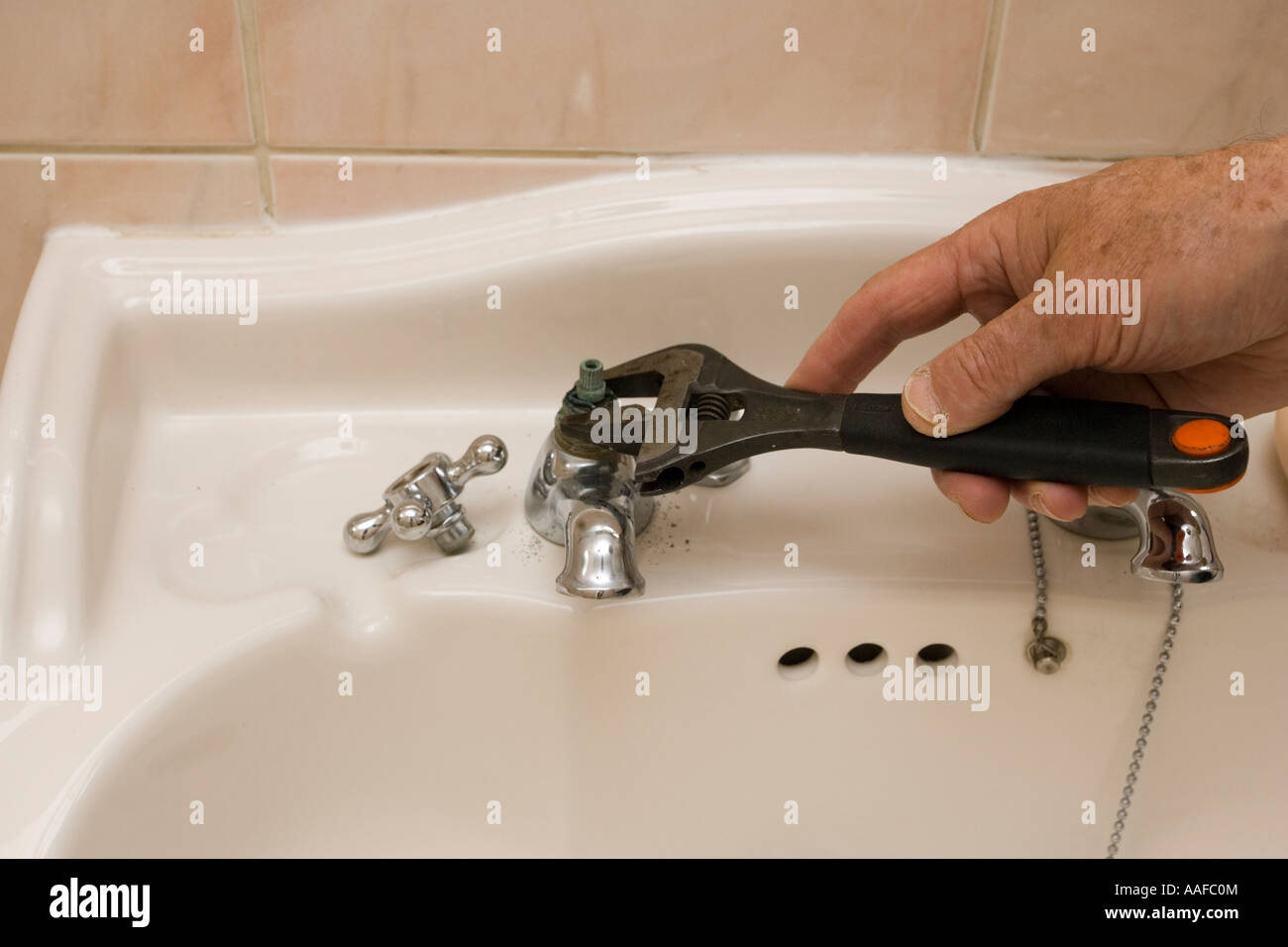 Hand with adjustable spanner repairing leaking bathroom basin tap UK