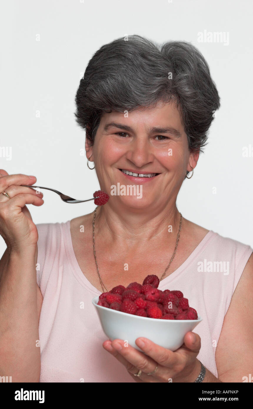 Mature woman eating bowl of raspberries portrait close up Stock Photo ...