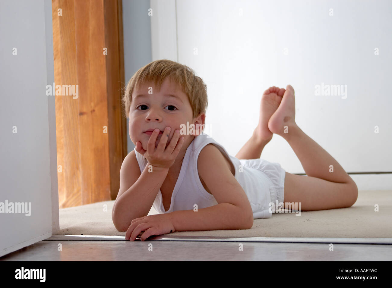 Young boy child in vest and underpants lying on his tummy looking